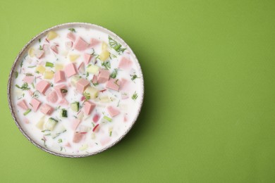 Photo of Delicious cold summer soup (okroshka) with boiled sausage in bowl on green table, top view. Space for text