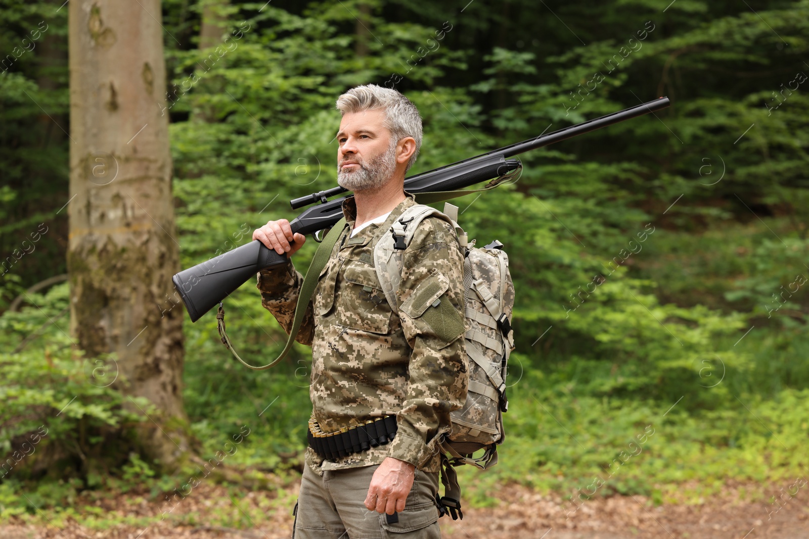 Photo of Man with hunting rifle and backpack wearing camouflage in forest