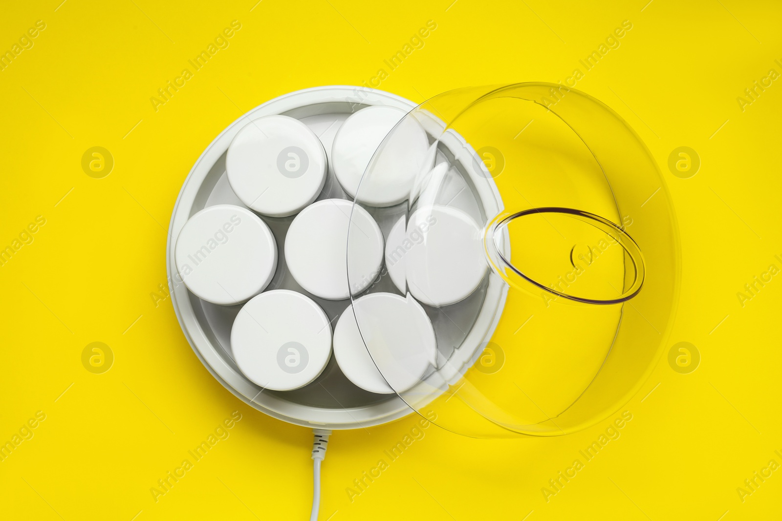 Photo of Modern yogurt maker with jars on yellow background, top view