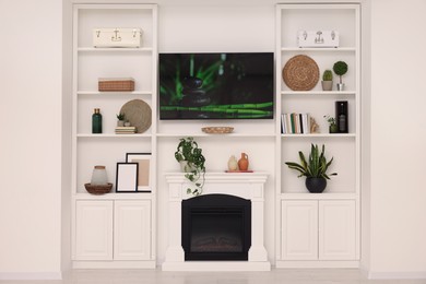 Photo of TV, fireplace and shelves with different decor in room. Interior design