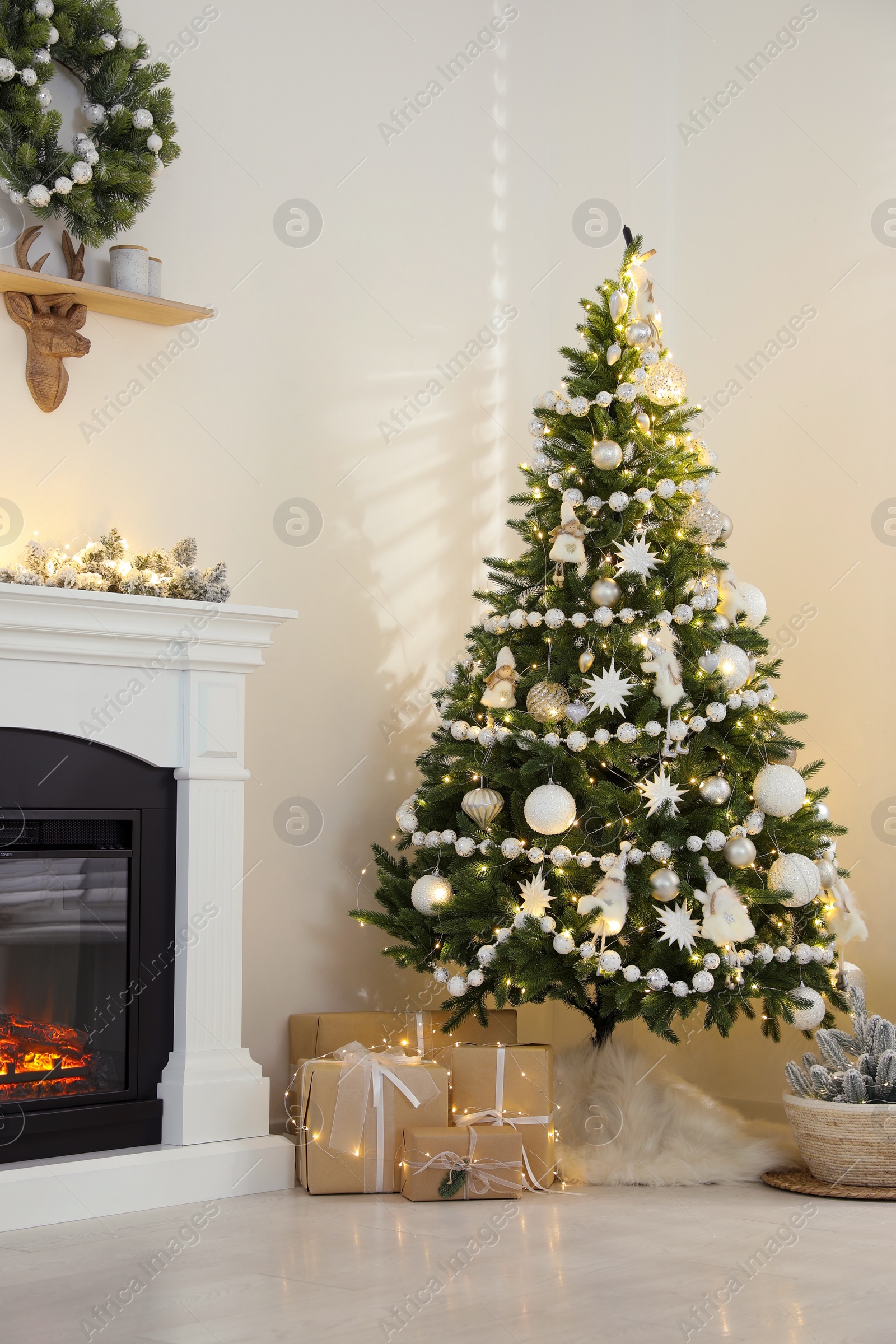 Photo of Decorated Christmas tree with faux fur skirt and gift boxes near fireplace indoors