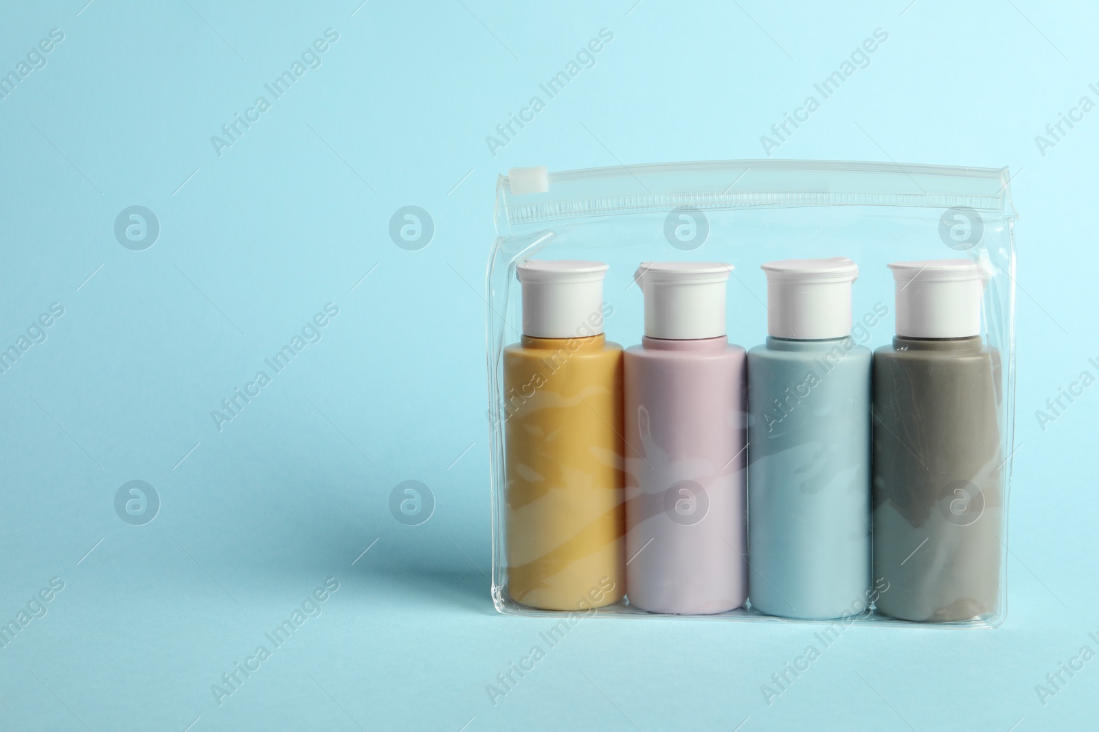 Photo of Cosmetic travel kit in plastic bag on light blue background. Space for text