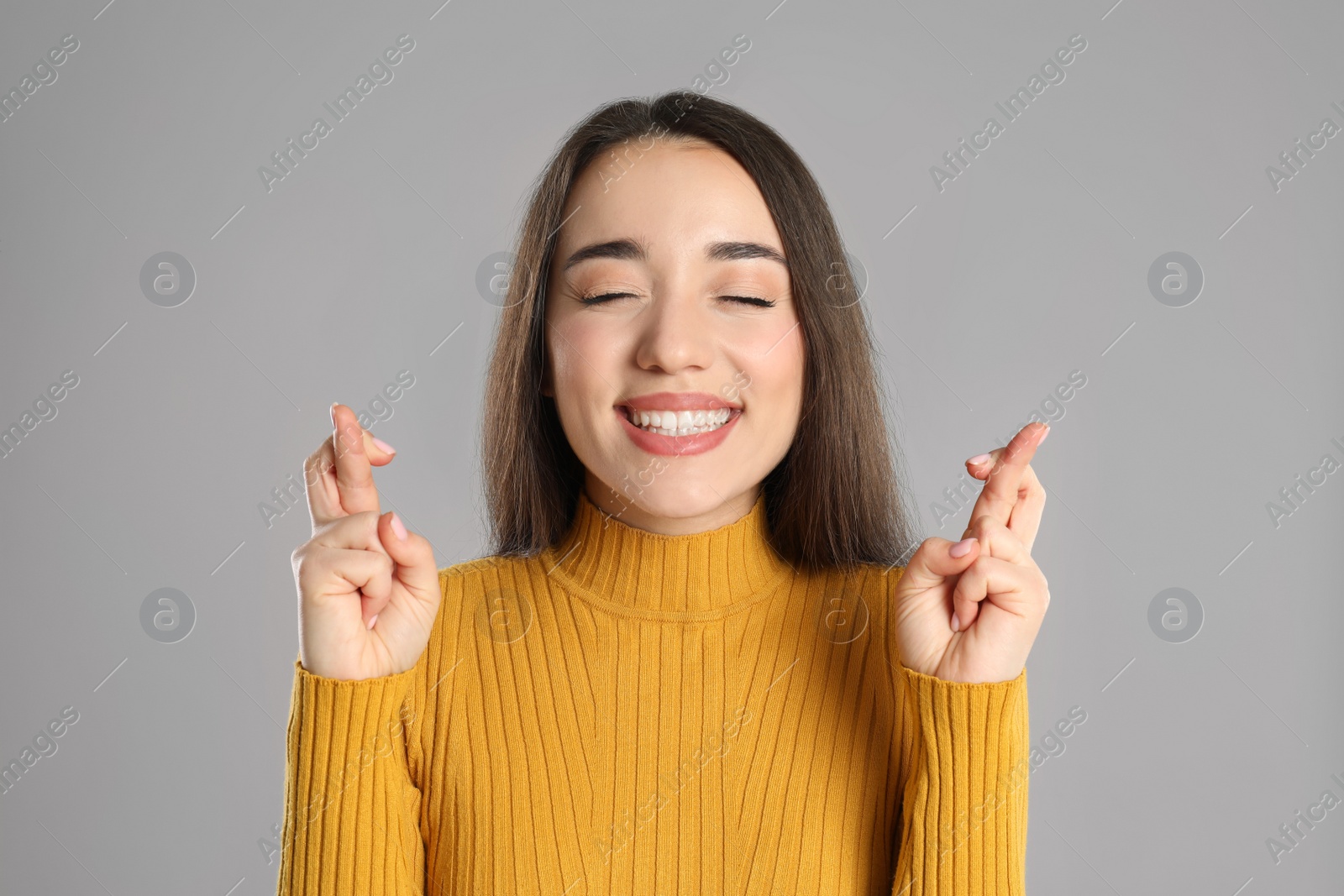 Photo of Excited young woman holding fingers crossed on grey background. Superstition for good luck