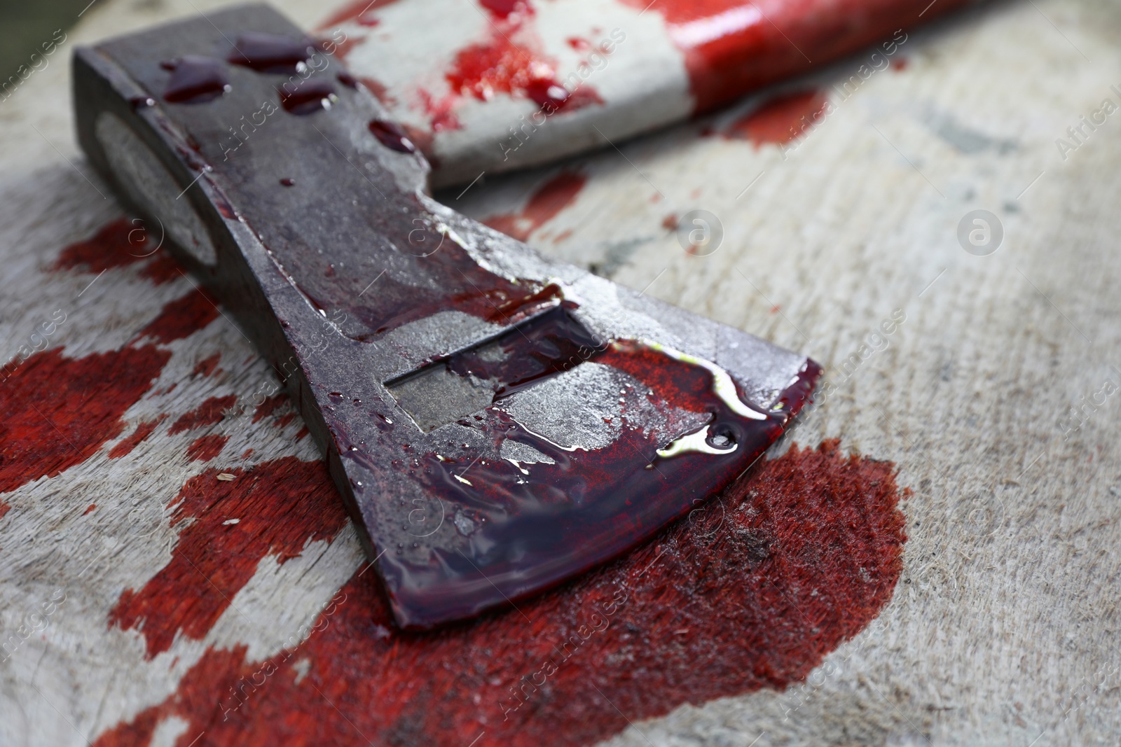 Photo of Axe with blood on wooden surface, closeup