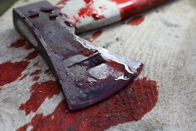 Axe with blood on wooden surface, closeup