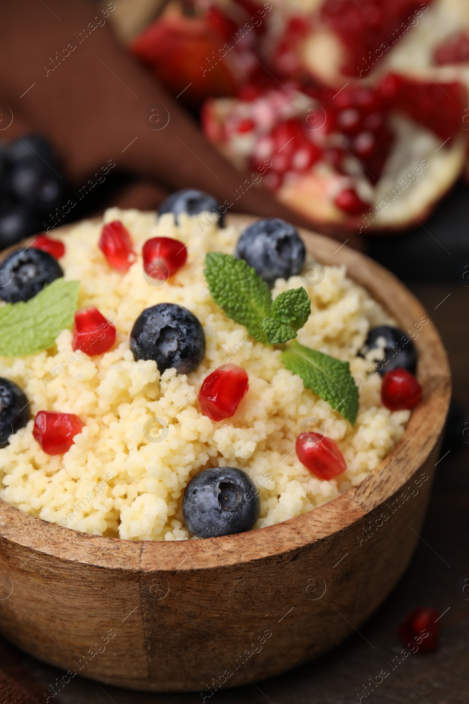 Photo of Bowl of tasty couscous with blueberries, pomegranate and mint on table, closeup
