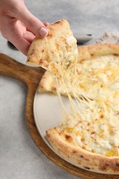 Photo of Woman taking piece of delicious cheese pizza at light grey table, closeup