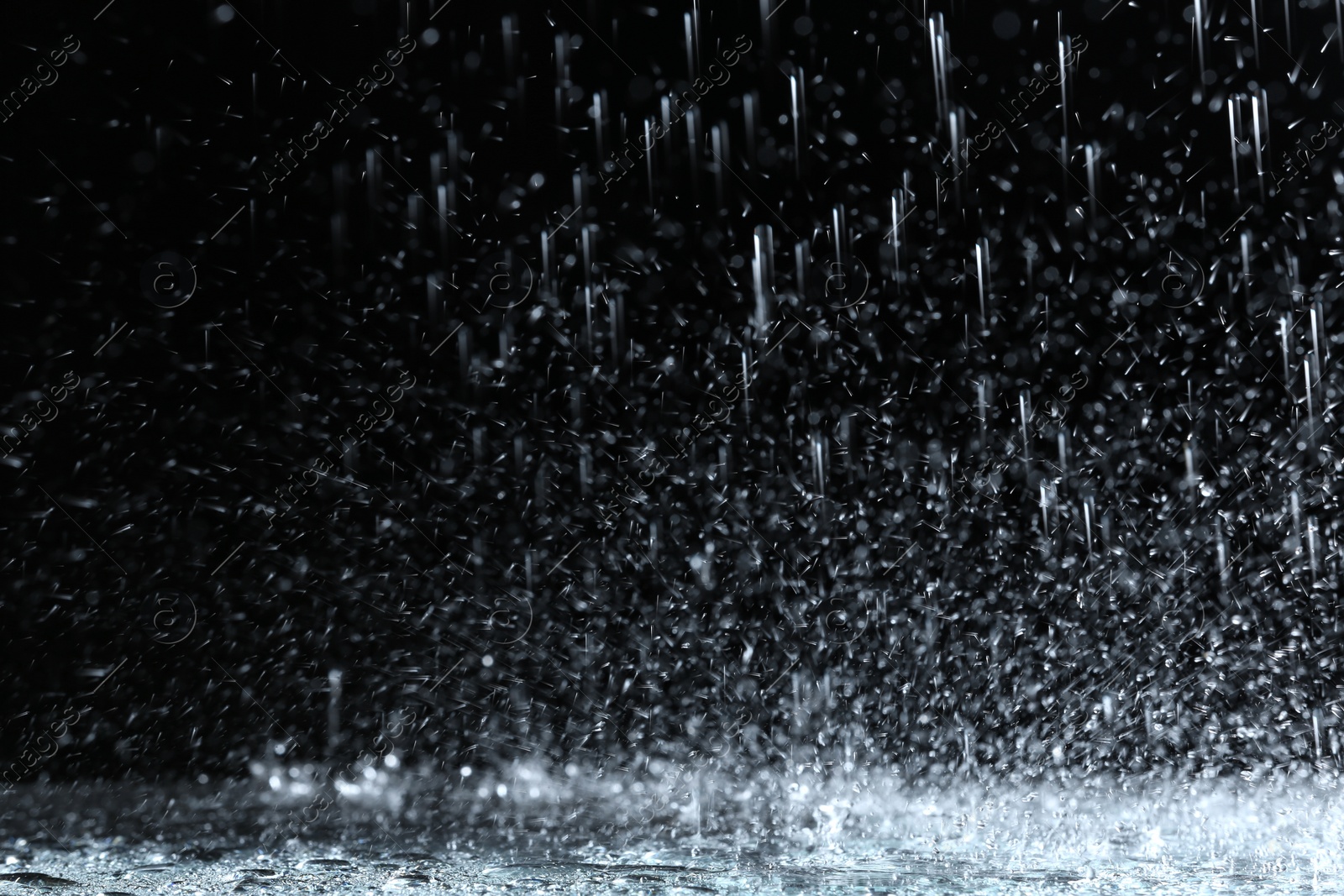 Photo of Heavy rain falling down on ground against dark background