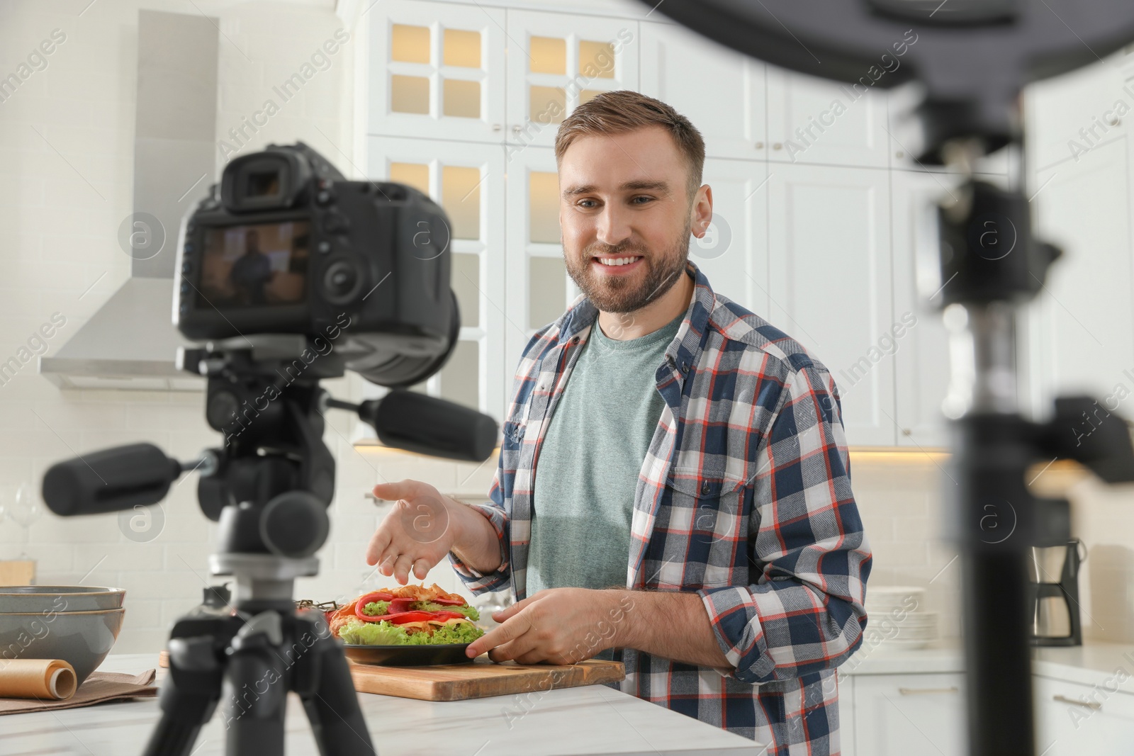 Photo of Blogger with tasty croissant recording video in kitchen at home. Using ring lamp and camera