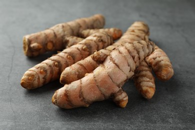 Photo of Many raw turmeric roots on grey table, closeup