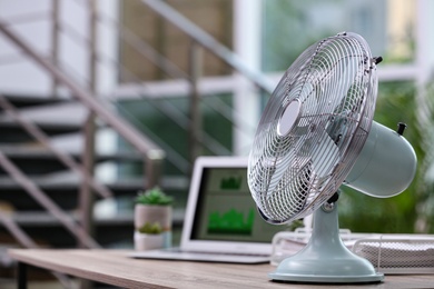 Photo of Modern electric fan on table in office. Space for text