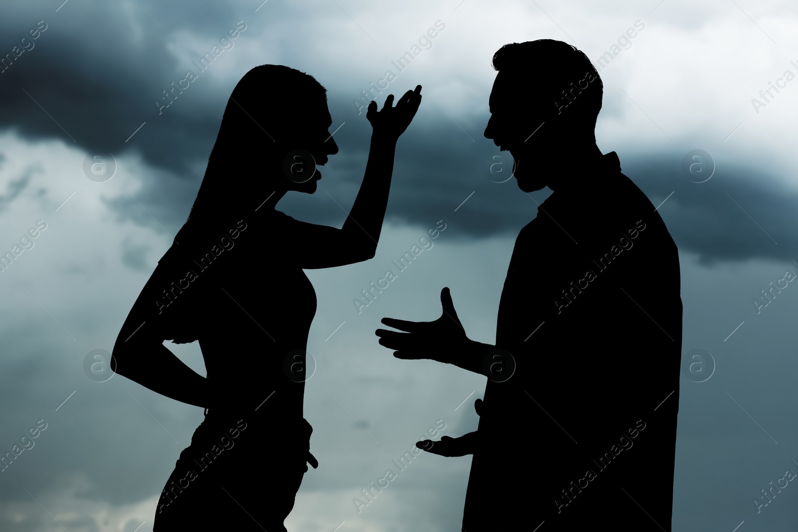 Image of Silhouettes of arguing couple against sky with heavy rainy clouds. Relationship problems