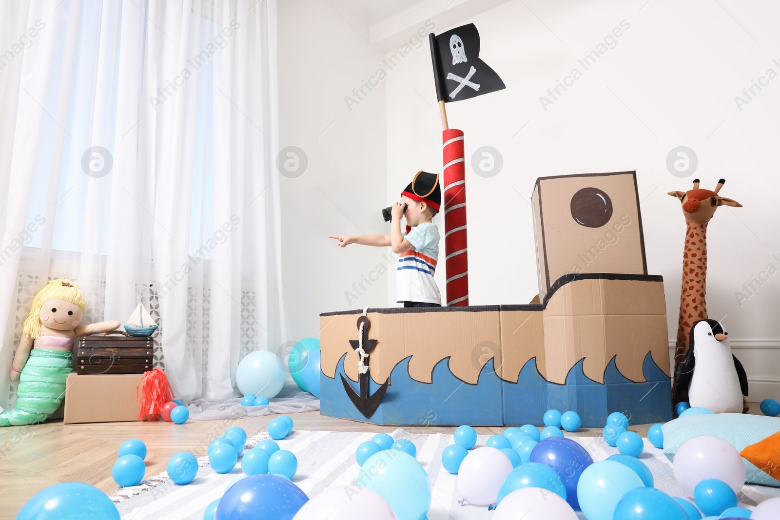Photo of Little boy playing with binoculars in pirate cardboard ship at home. Child's room interior