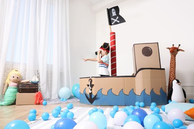 Photo of Little boy playing with binoculars in pirate cardboard ship at home. Child's room interior