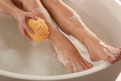 Photo of Woman rubbing her leg with sponge while taking bath, closeup