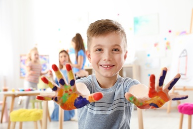 Photo of Cute little child showing painted hands at lesson indoors