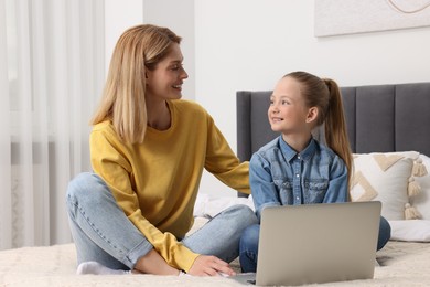 Photo of Happy woman and her daughter with laptop on bed at home