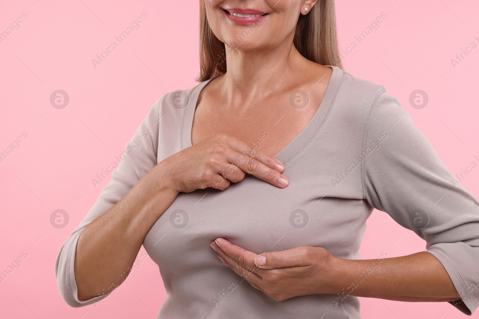 Photo of Woman doing breast self-examination on pink background, closeup