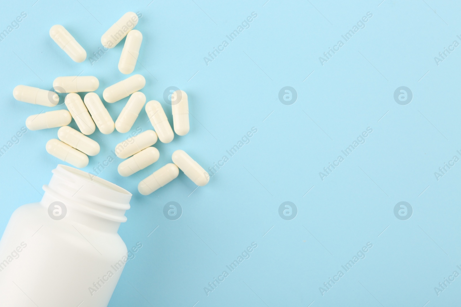 Photo of Bottle and vitamin capsules on light blue background, top view. Space for text