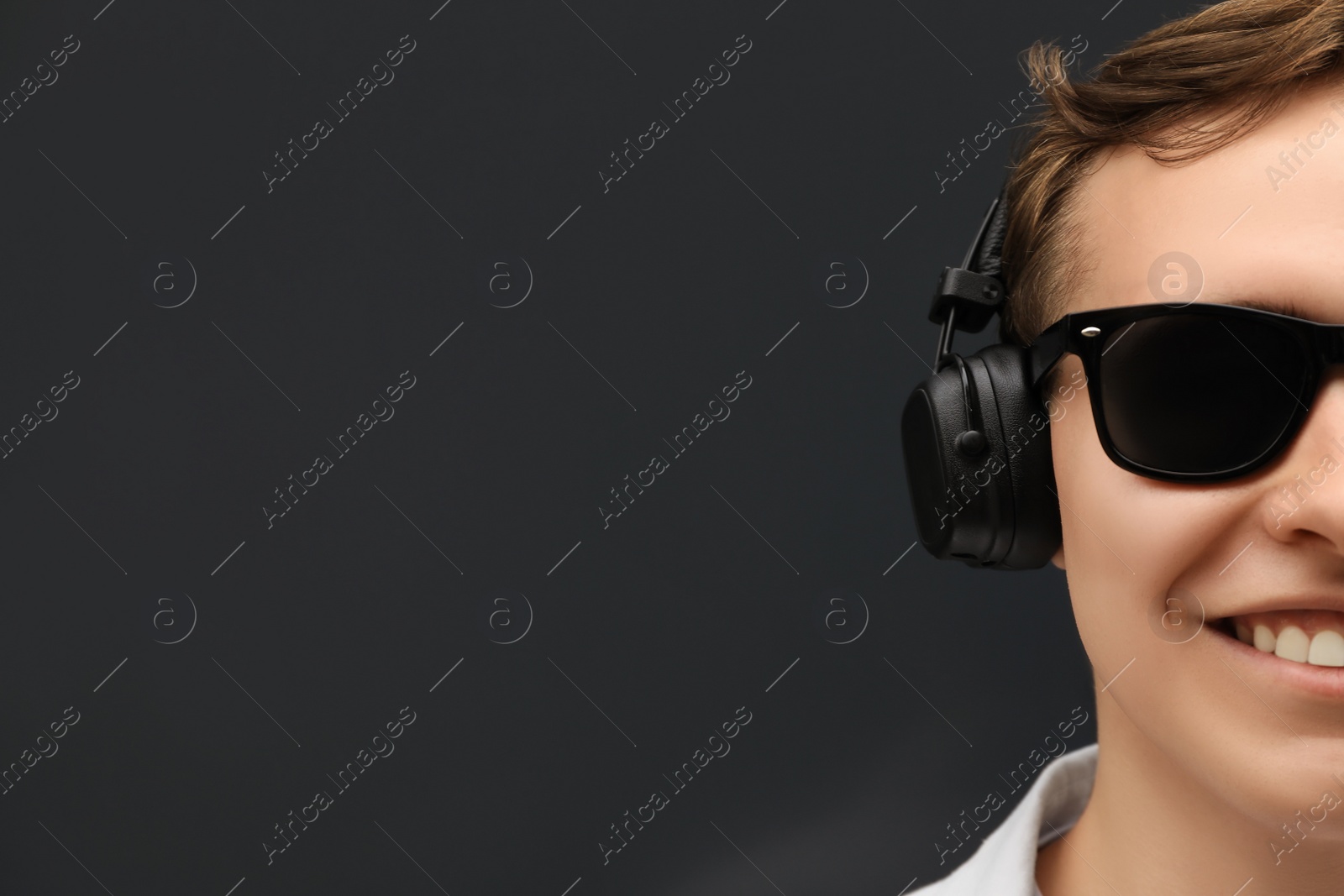 Photo of Handsome young man with headphones near black wall, closeup. Space for text