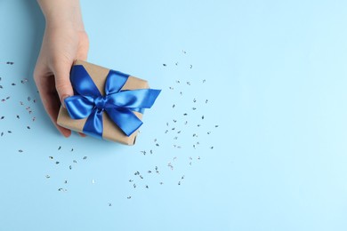 Photo of Woman with gift box and confetti on light blue background, top view. Space for text