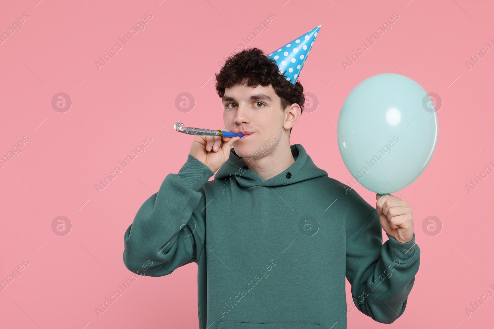 Photo of Young man in party hat with blower and balloon on pink background