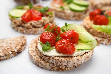 Photo of Crunchy buckwheat cakes with cream cheese, tomatoes and cucumber slices on white table, closeup