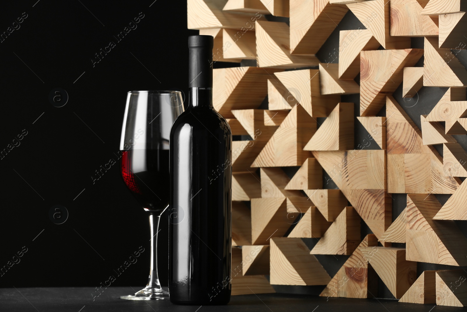 Photo of Stylish presentation of red wine in bottle and wineglass on table against black background