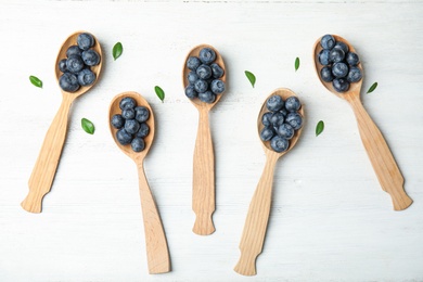 Flat lay composition of spoons with tasty blueberries on white wooden table