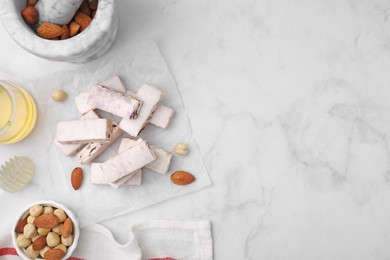 Photo of Pieces of delicious nutty nougat, nuts and honey on white marble table, flat lay. Space for text