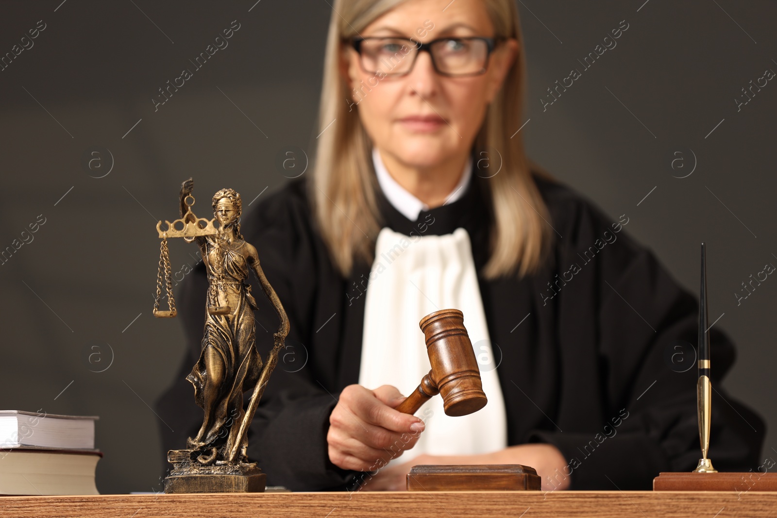 Photo of Judge striking mallet at wooden table, selective focus. Figure of Lady Justice indoors