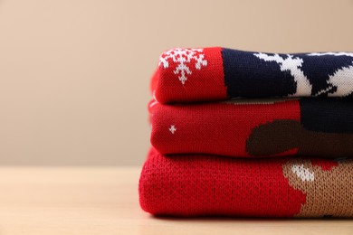 Stack of different Christmas sweaters on table against beige background. Space for text