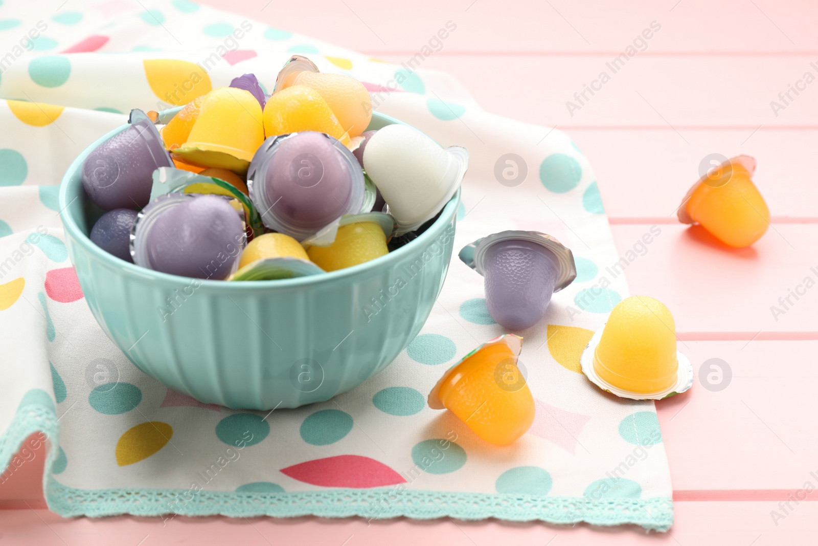 Photo of Bowl with tasty bright jelly cups on pink wooden table