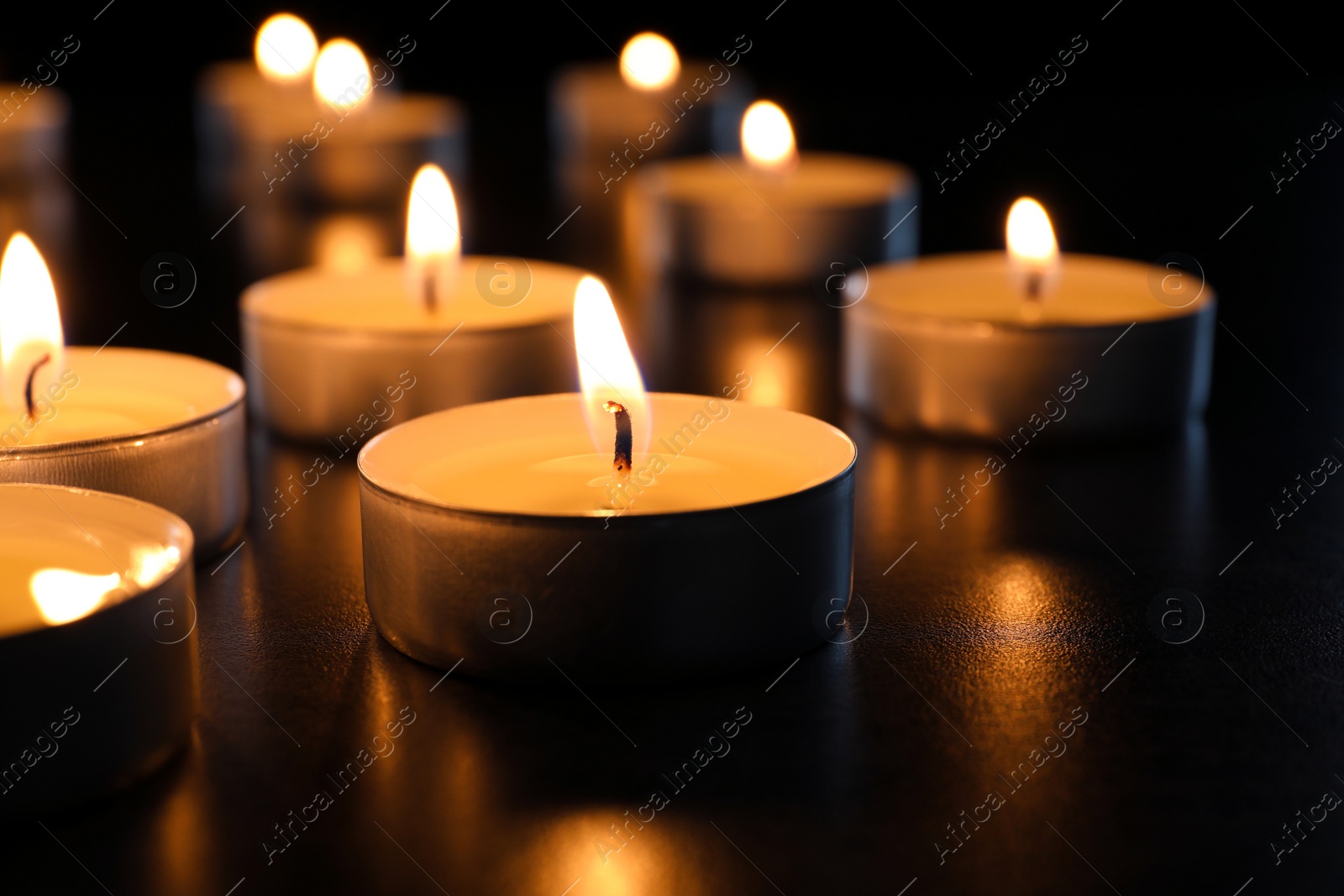 Photo of Wax candles burning on table in darkness, closeup