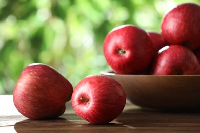 Ripe red apples and bowl on wooden table outdoors, closeup