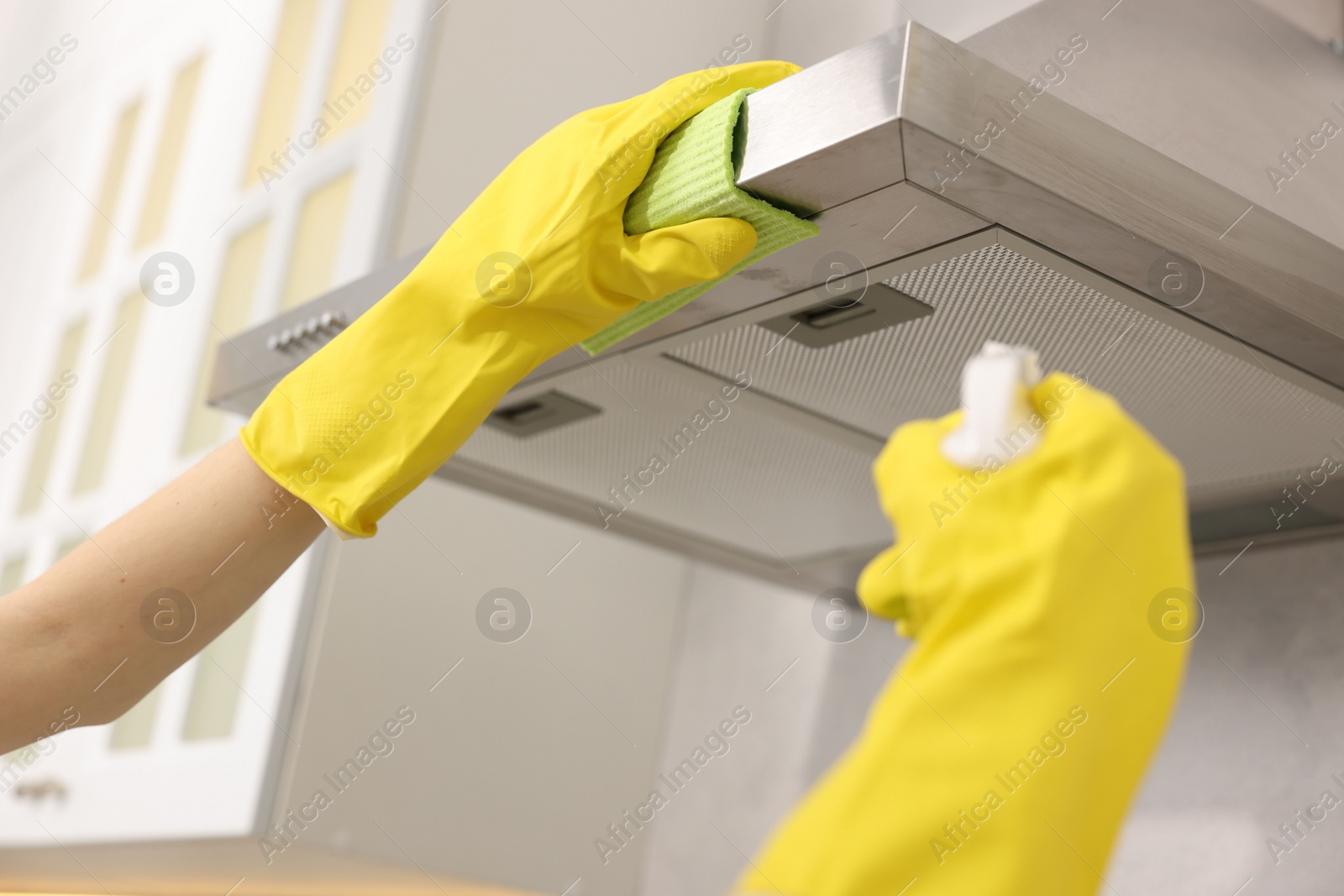 Photo of Woman with spray bottle and microfiber cloth cleaning kitchen hood indoors, closeup