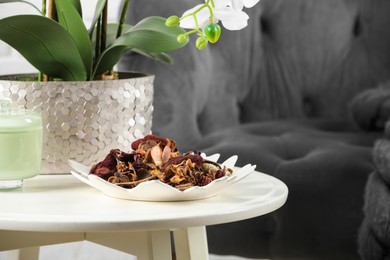Photo of Aromatic potpourri of dried flowers in plate and beautiful houseplant on white table indoors. Space for text