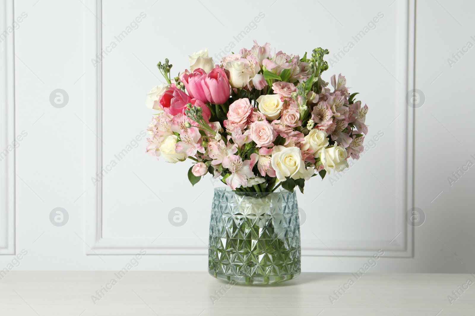 Photo of Beautiful bouquet of fresh flowers in vase on table near white wall