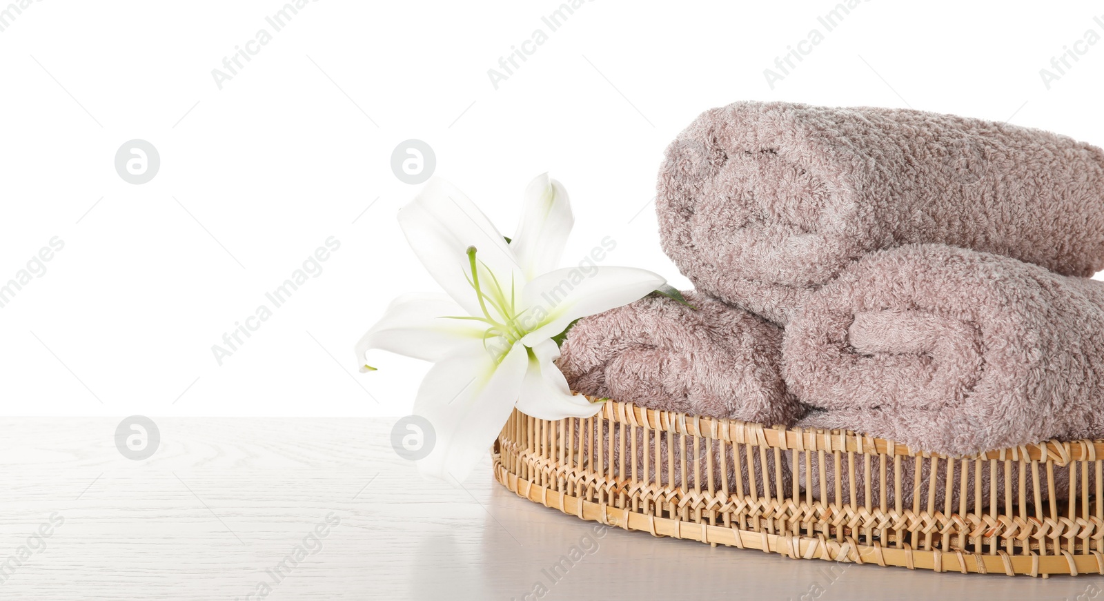 Photo of Fresh towels and lily flower on wooden table against white background. Space for text