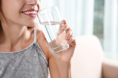 Woman drinking clean water from glass at home, closeup