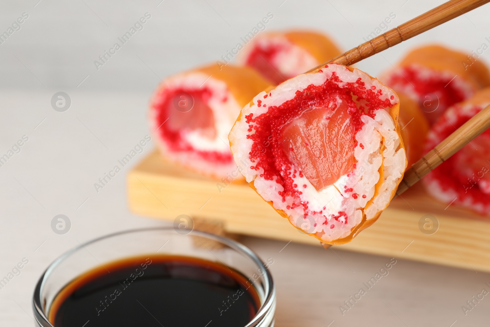 Photo of Holding delicious sushi roll with chopsticks at white table, closeup
