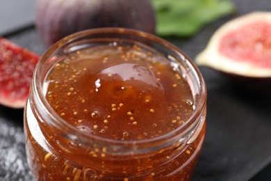Jar of tasty fig jam and fresh fruits on table, closeup
