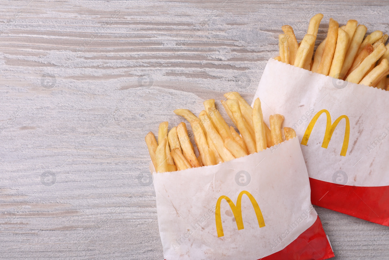 Photo of MYKOLAIV, UKRAINE - AUGUST 12, 2021: Two small portions of McDonald's French fries on white wooden table, flat lay. Space for text