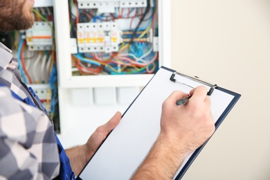Photo of Male electrician with clipboard near fuse board indoors, closeup