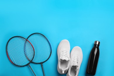 Photo of Rackets, sneakers and bottle on light blue background, flat lay with space for text. Playing badminton