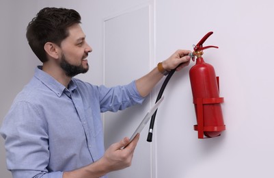 Man with tablet checking fire extinguisher indoors