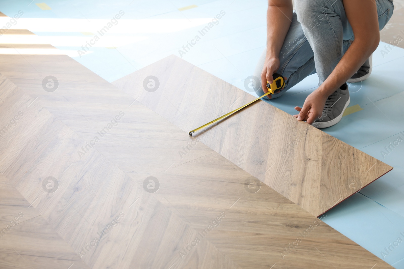 Photo of Worker installing laminated wooden floor indoors, closeup