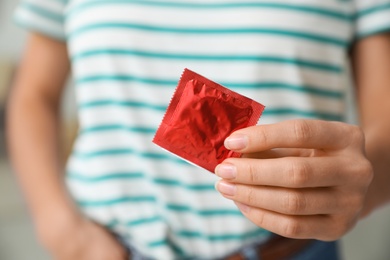 Woman holding condom indoors, closeup. Safe sex concept