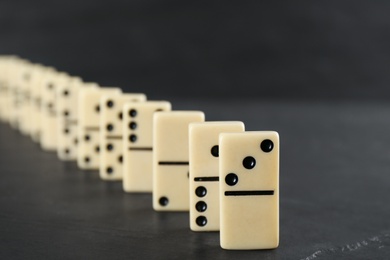 Photo of White domino tiles with black pips on dark grey table