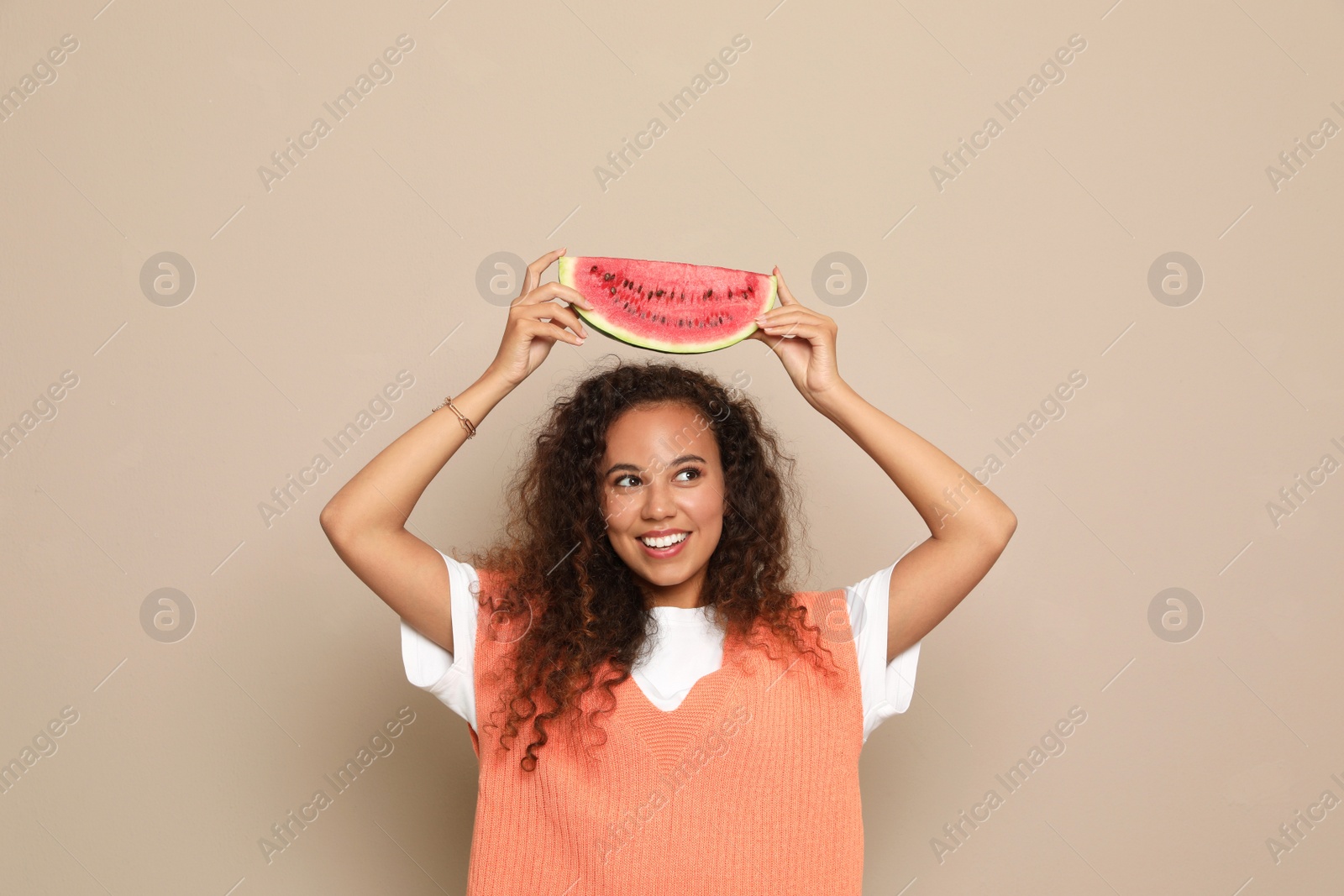 Photo of Beautiful young African American woman with slice of watermelon on beige background